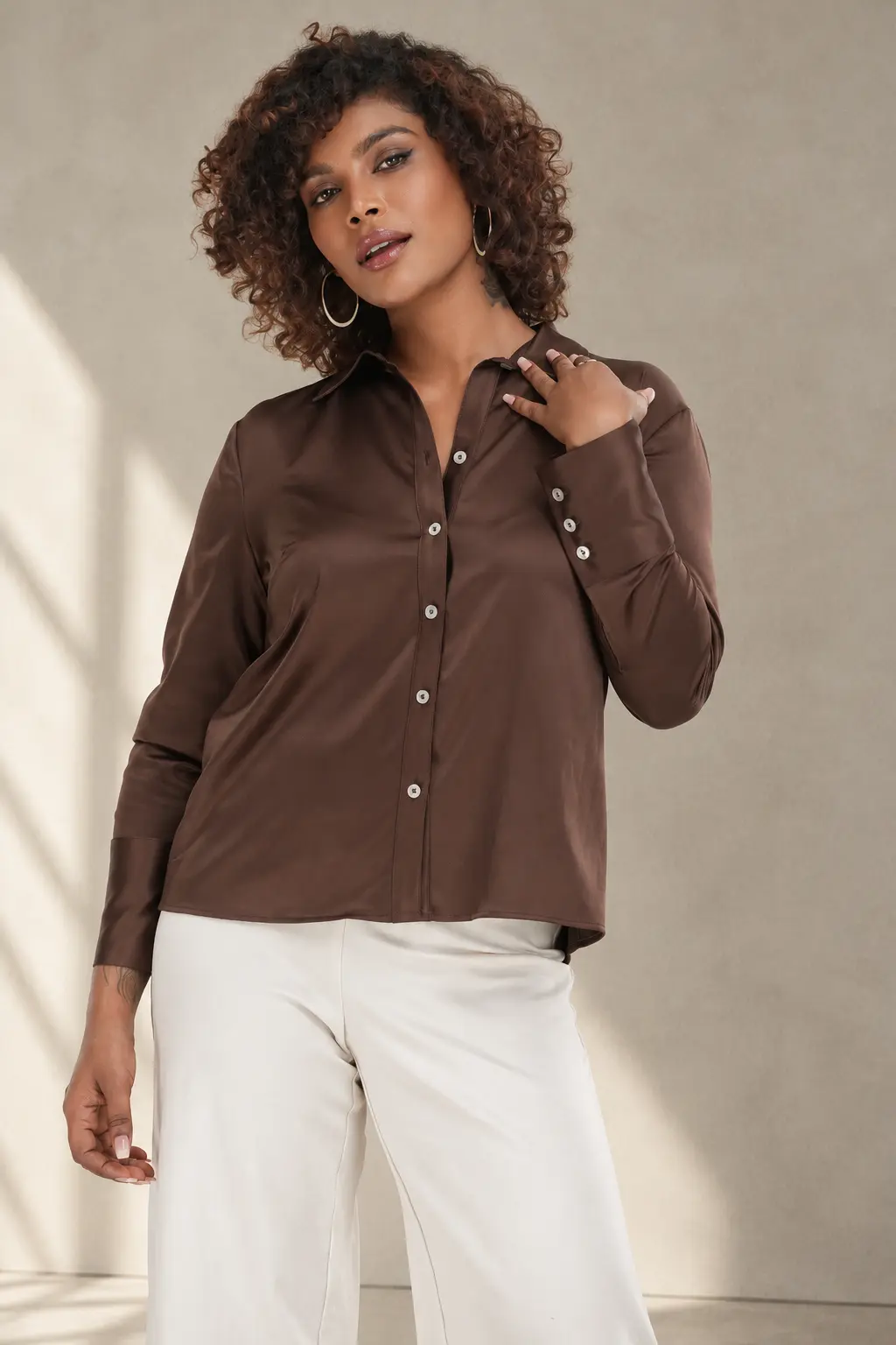 Model wearing a chocolate brown satin-finish button-down shirt with ivory wide-leg trousers, showcasing contemporary women's apparel by Trendyear
