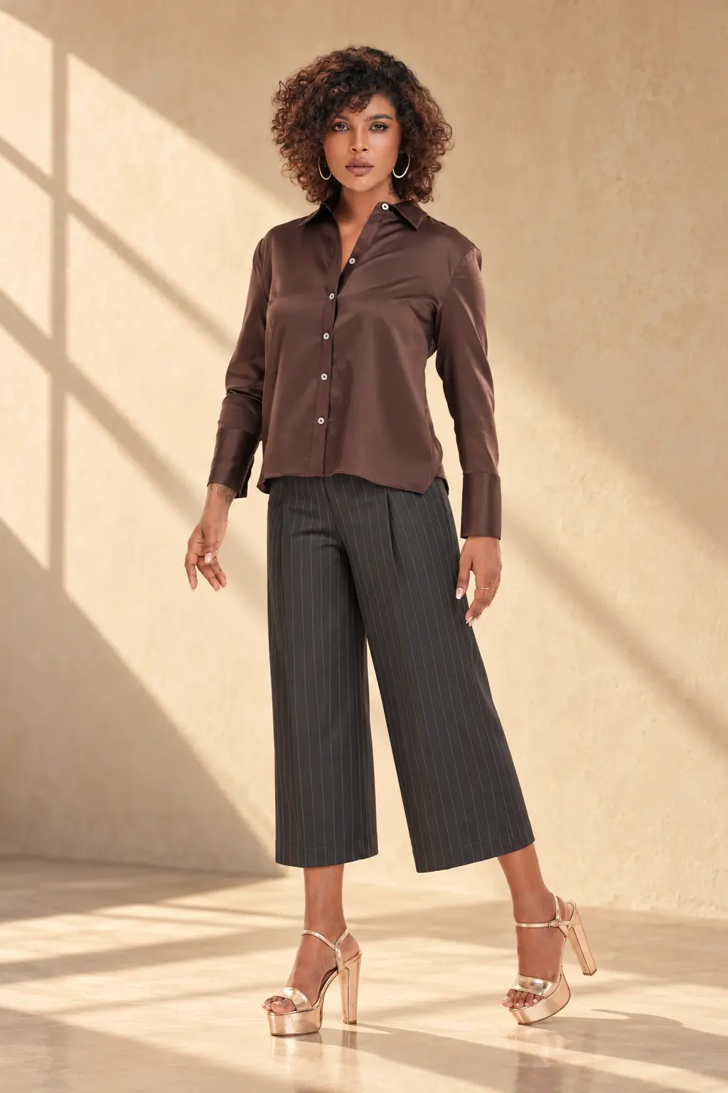 Model wearing a chocolate brown satin button-down shirt with charcoal pinstripe wide-leg culottes, featuring modern women's tailored apparel by Trendywear