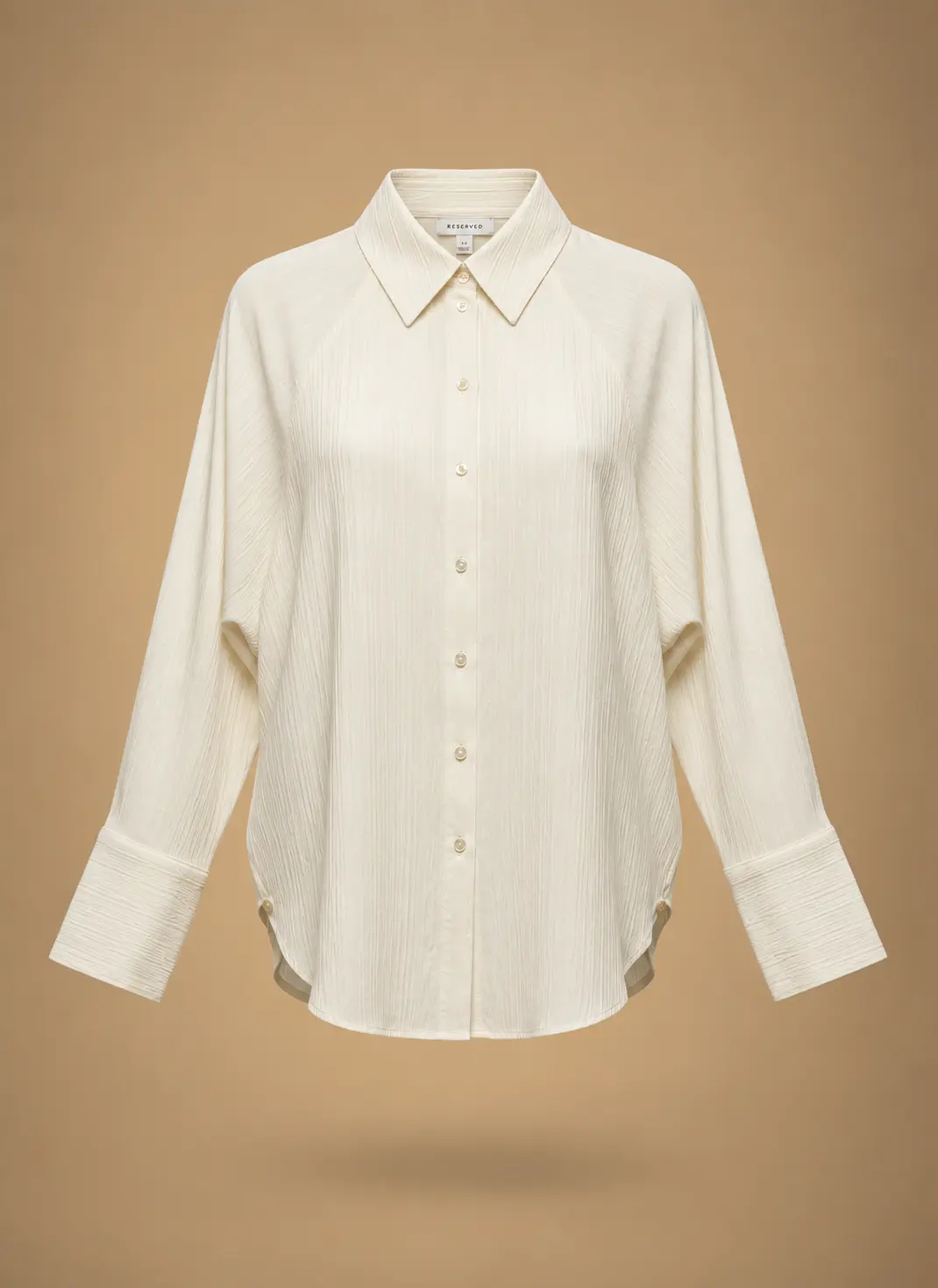 Ivory women's long-sleeve button-down blouse with subtle textured fabric, classic pointed collar, wide cuffs and curved hem